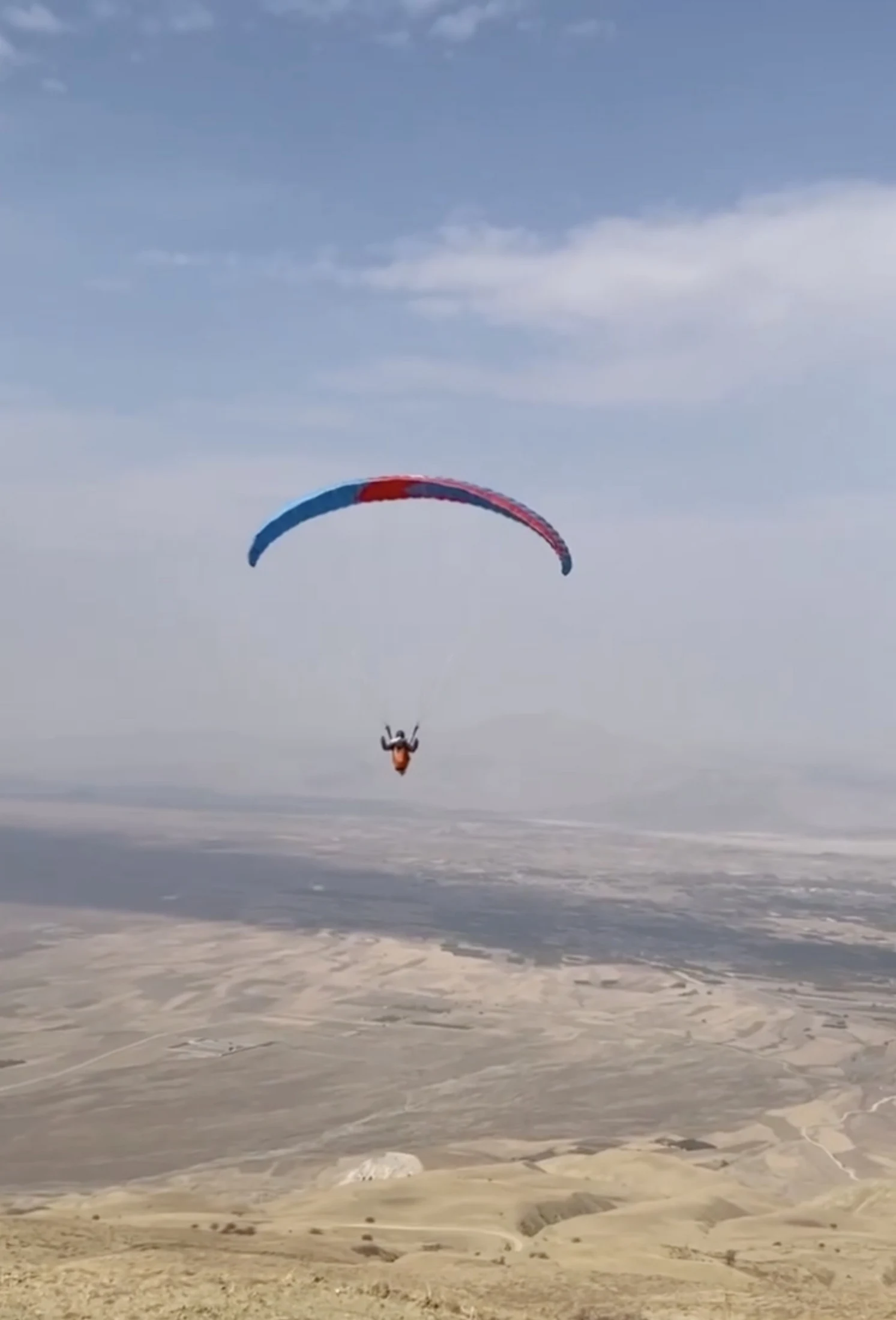Eine Gleitschirmfliegerin über einer weiten Landschaft.