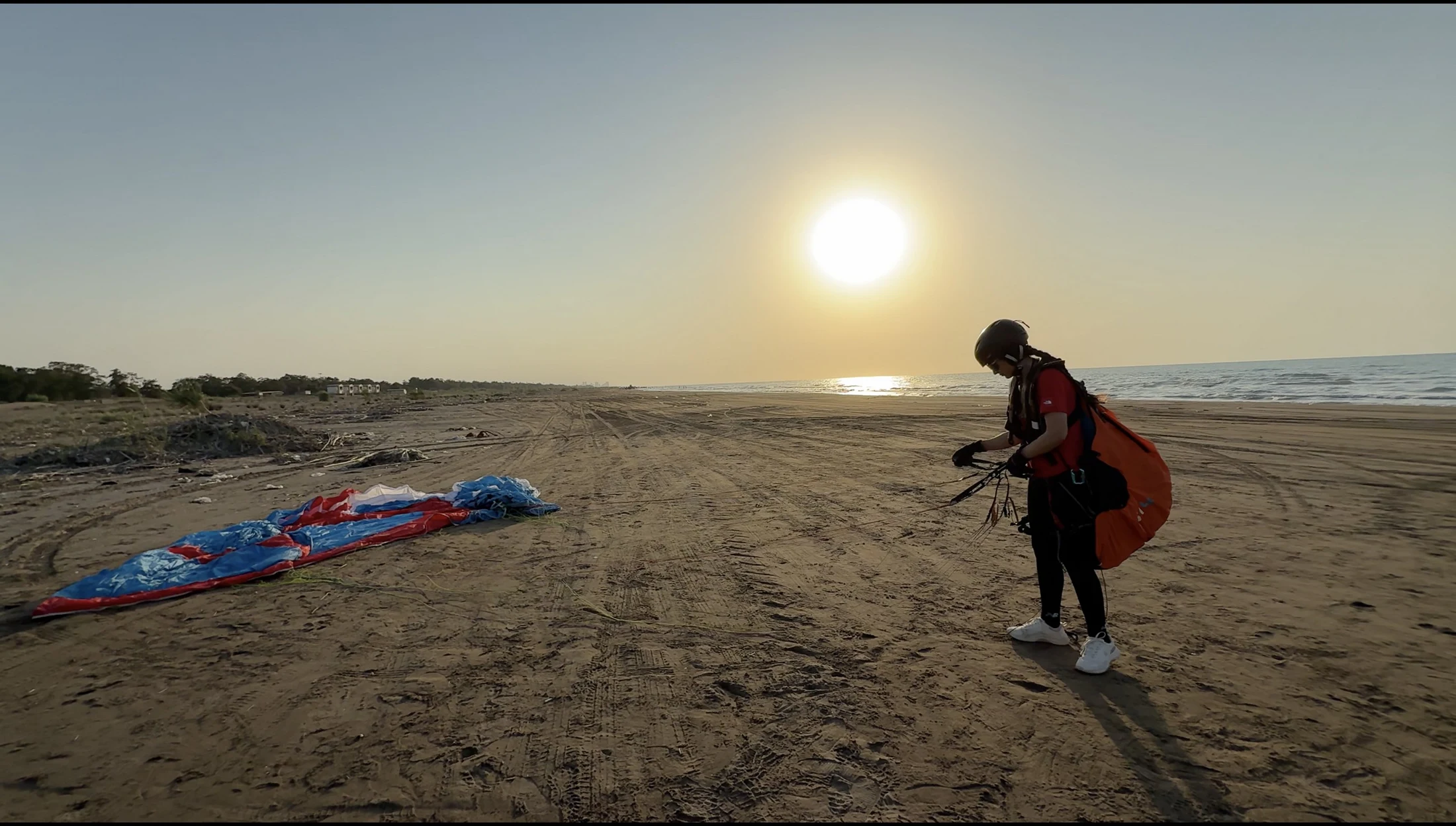 Eine Gleitschirmfliegerin prüft die Leinen am Strand.