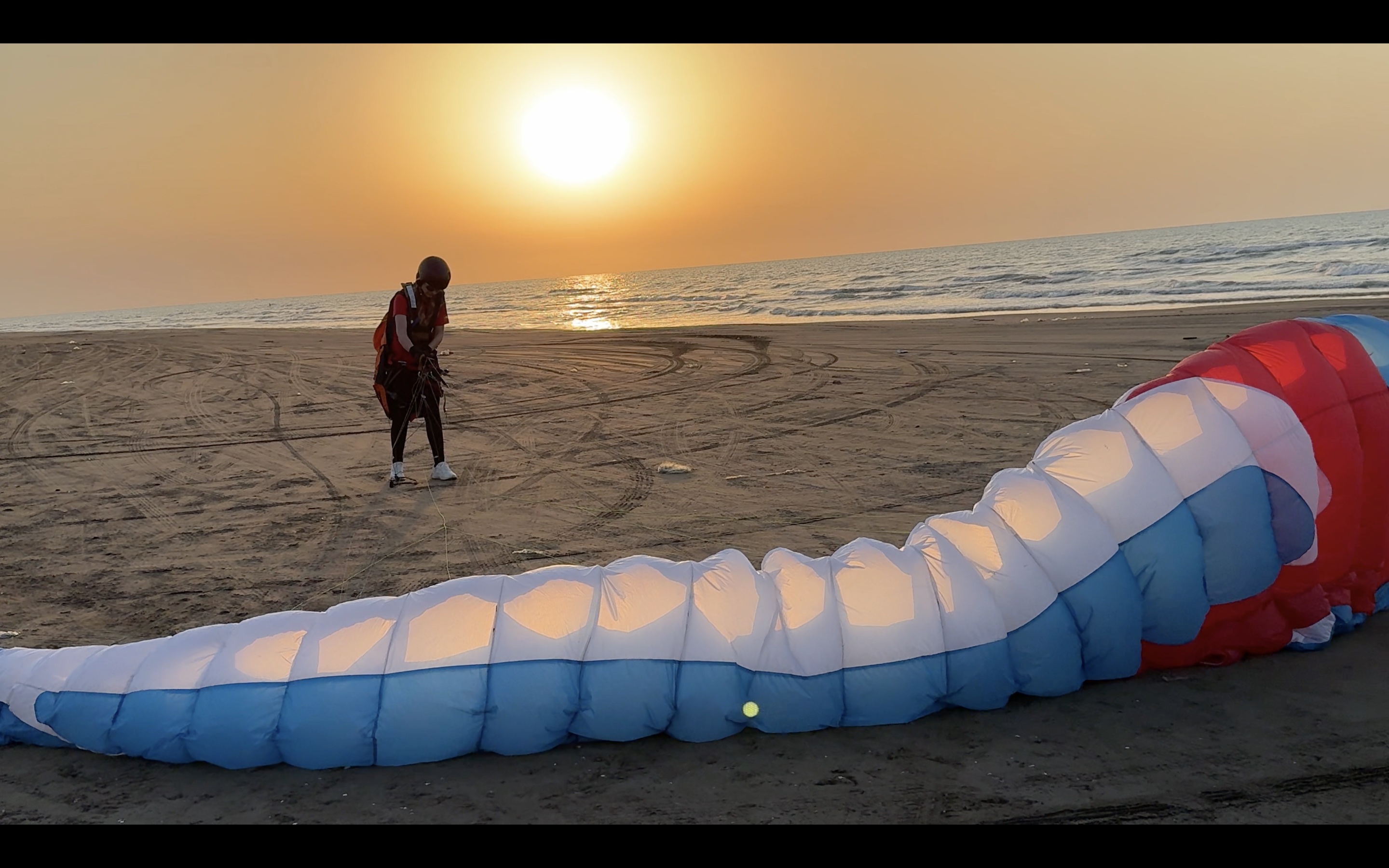 A paraglider preparing for flight on a beach at sunset